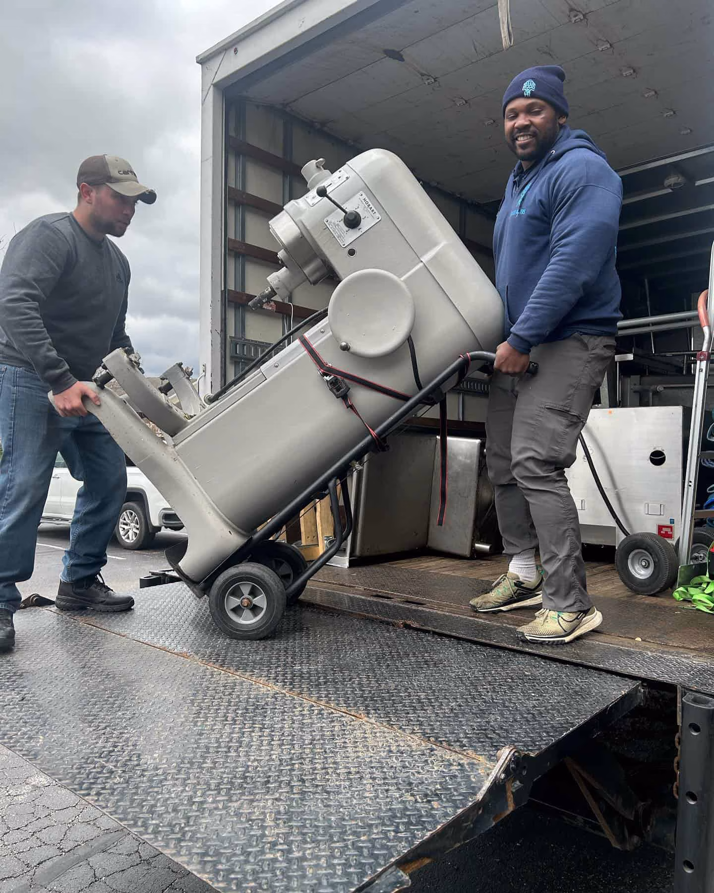 Two men loading industrial mixer into truck.