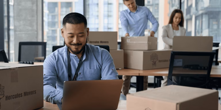Office employees packing boxes, working on laptops.